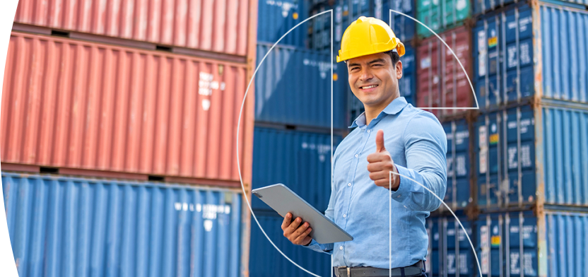 Foto de um homem em frente a containers usando um capacete e segurando uma prancheta e fazendo sinal de positivo com o dedão